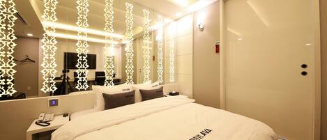 Habitación de hotel con una cama grande, una mesita de noche con teléfono, un espejo y un armario.