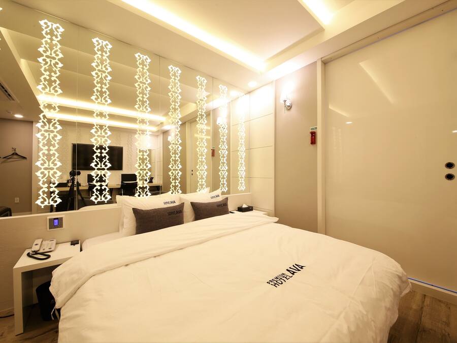 A hotel room with a large bed, a bedside table with a phone, a mirror, and a wardrobe.