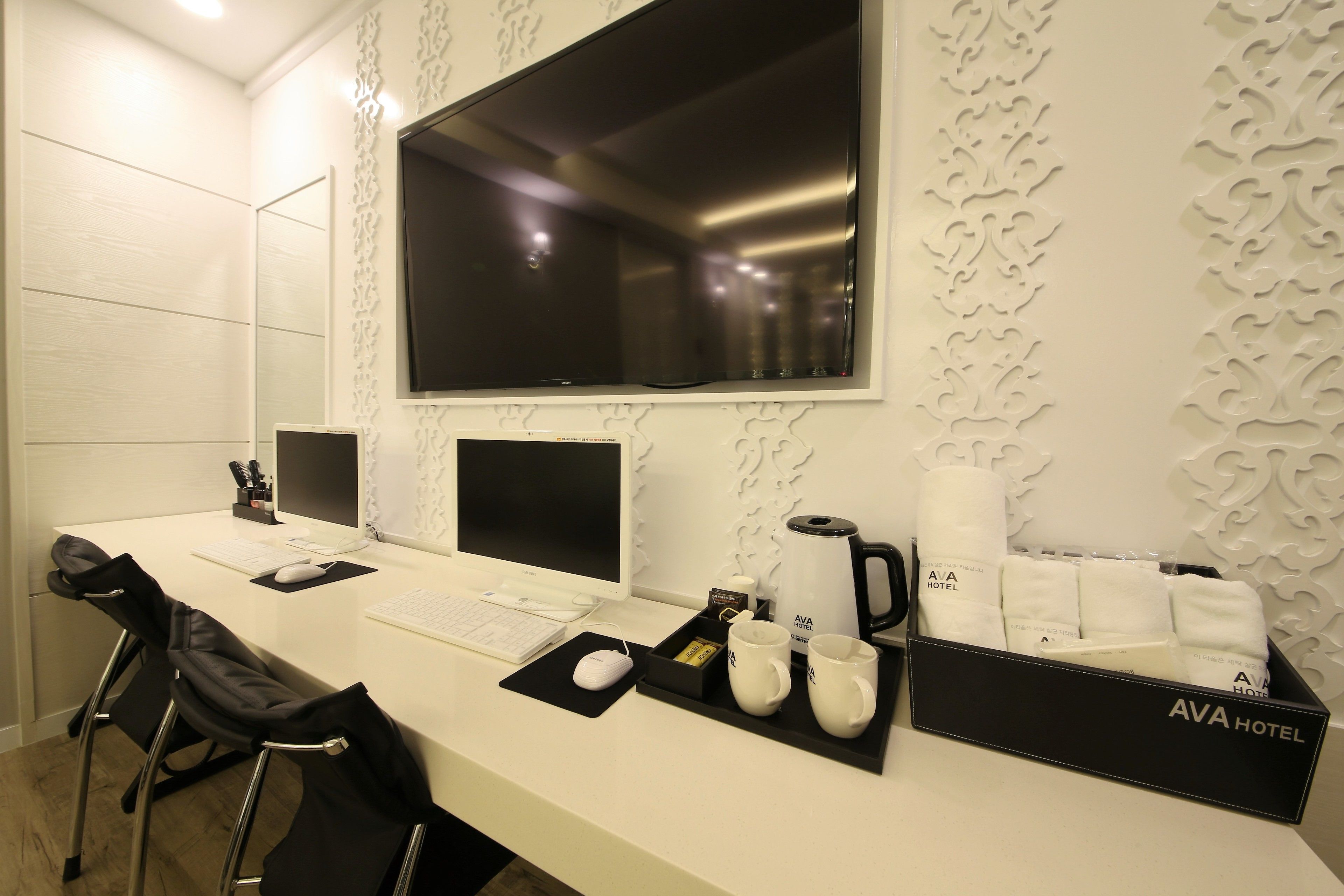 A hotel reception desk with two computer monitors, a keyboard, a mouse, a coffee maker, and a tray with towels and a coffee pot.