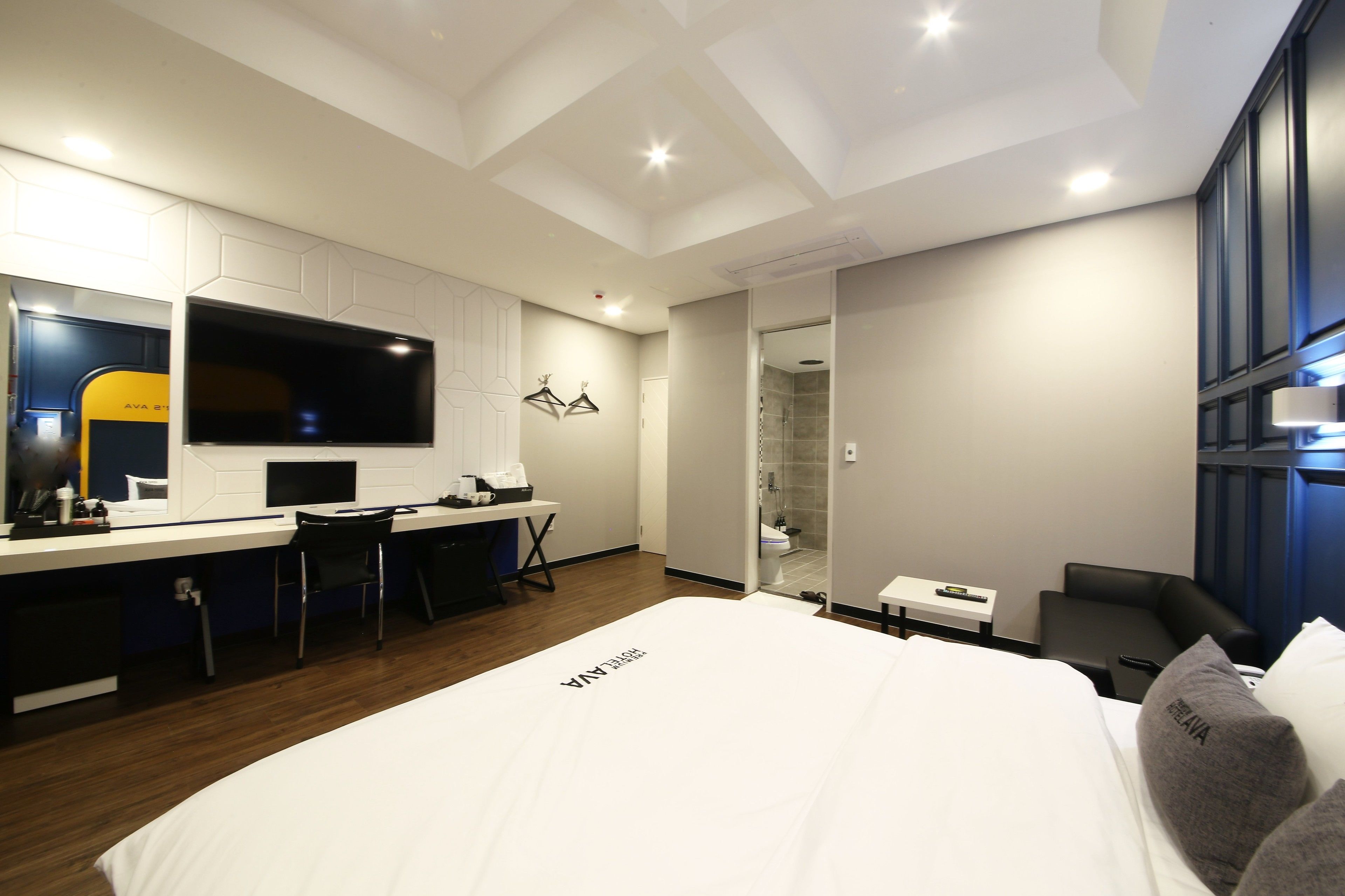 A modern hotel room with a large bed, a desk with a chair, a TV, and a shower area.