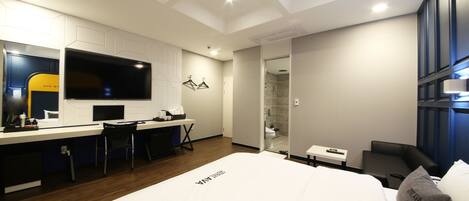 A modern hotel room with a large bed, a desk with a chair, a TV, and a shower area.