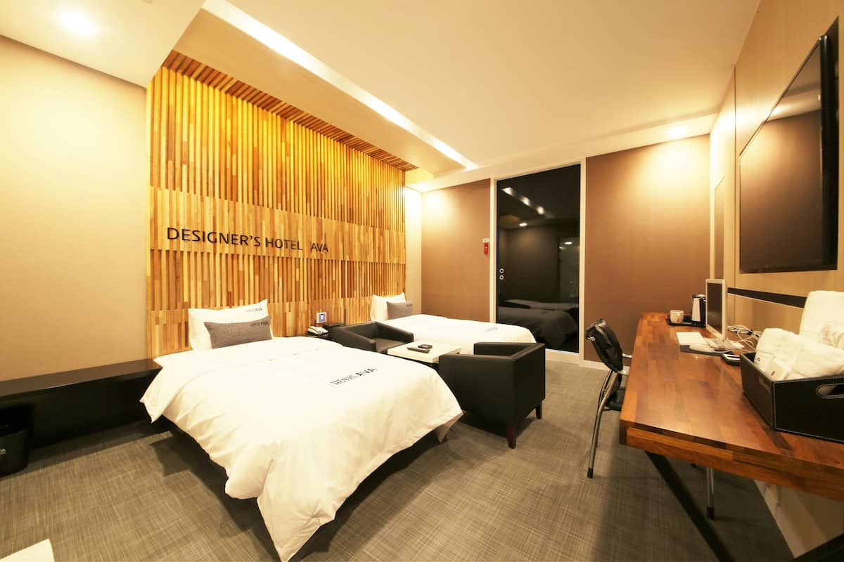 Habitación de hotel con dos camas, un escritorio, una silla y un televisor.