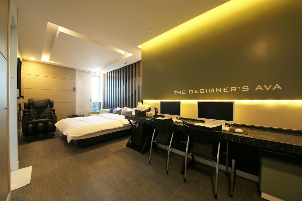 Una habitación de hotel moderna con cama, sillón de masajes, escritorio con dos sillas y un espejo grande.