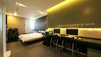 A modern hotel room with a bed, a massage chair, a desk with two chairs, and a large mirror.