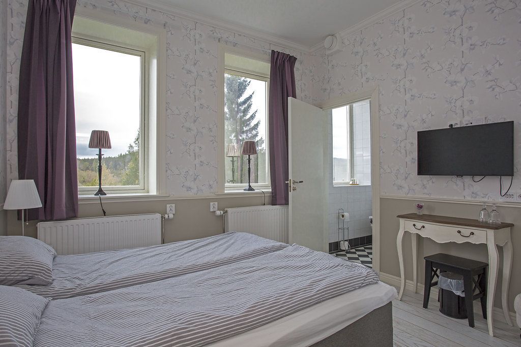 Un dormitorio con dos camas, un aparador, un televisor y una ventana con cortinas.