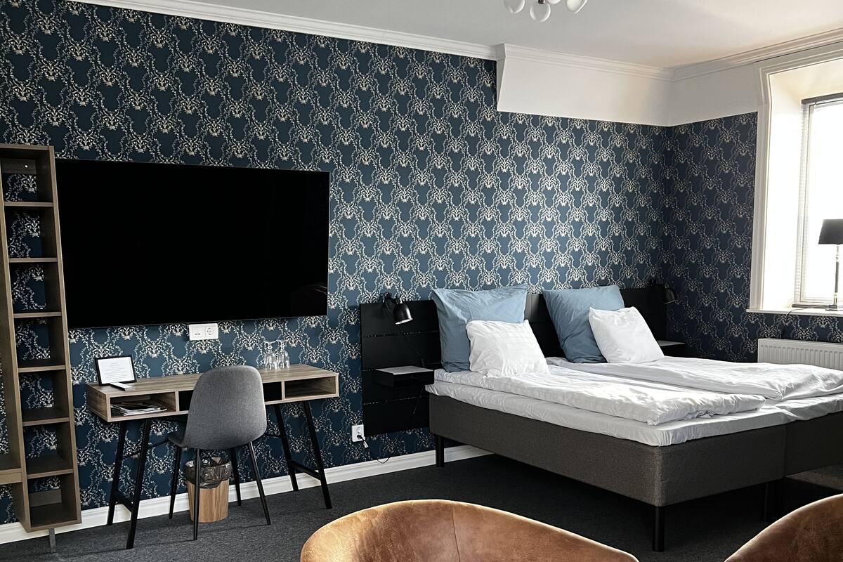 A modern bedroom with a large bed, a desk, and two chairs.