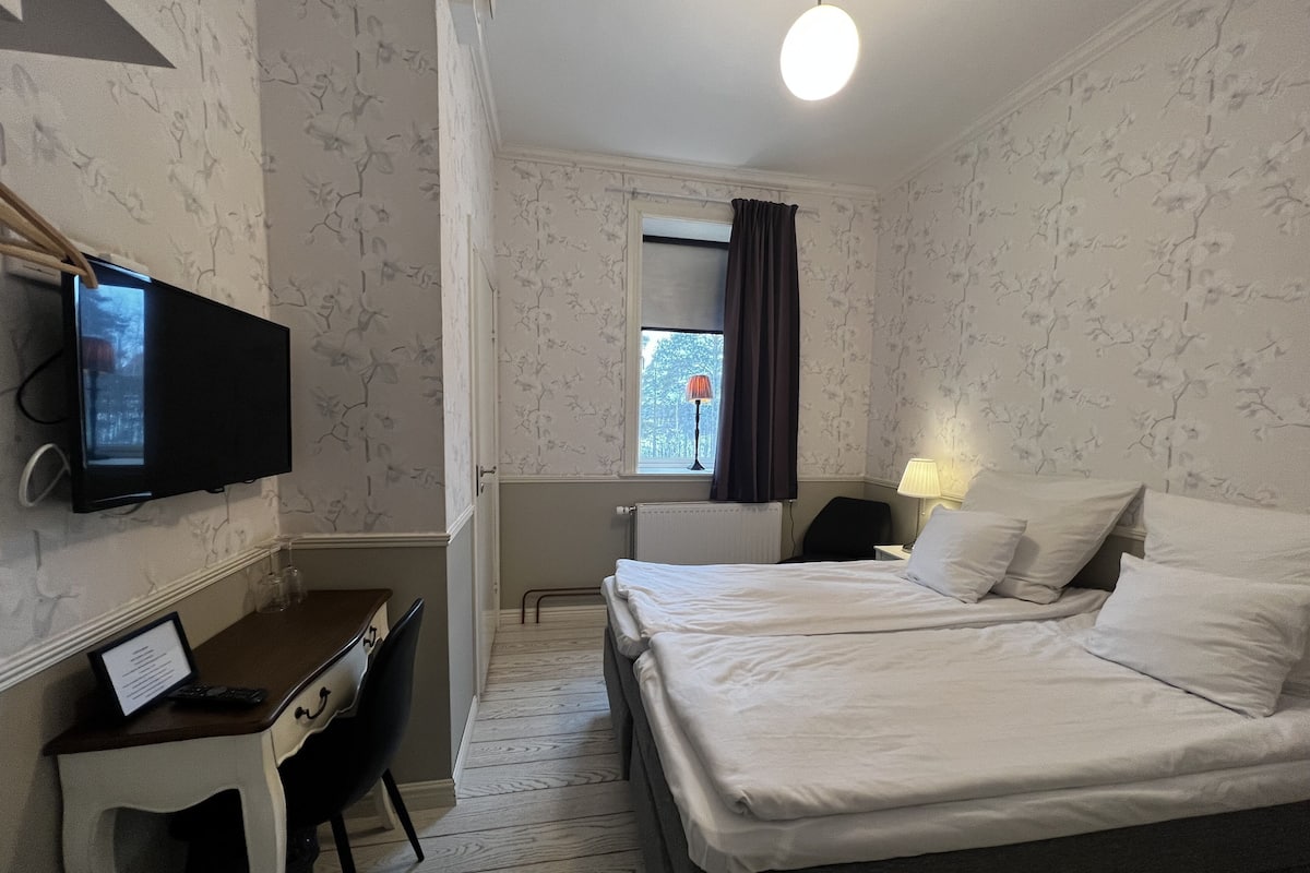 A hotel room with a bed, desk, chair, TV, and a window with curtains.