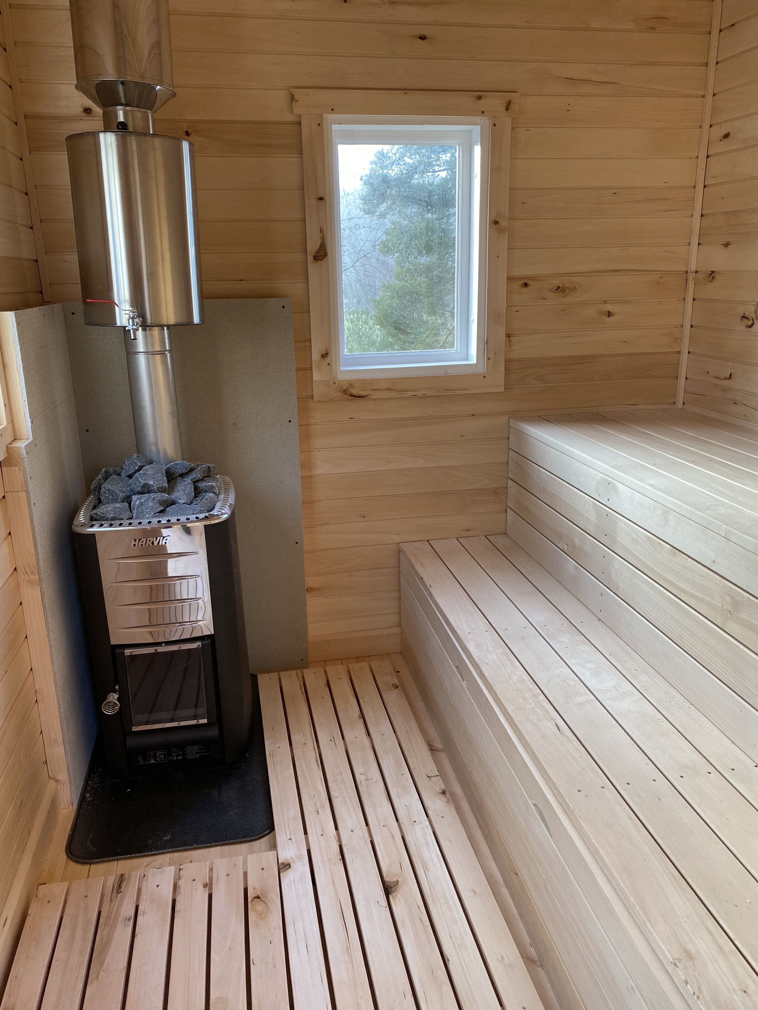 Una cabaña de madera con estufa de leña, una ventana y un banco.