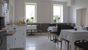 A dining area with tables and chairs, a kitchen area with cabinets and appliances, and large windows providing natural light. - Norrfly Herrgård AB (Kilafors)