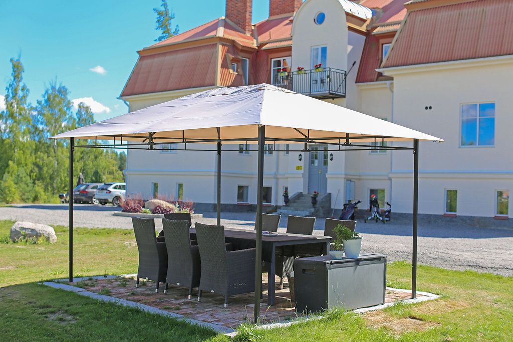 Un patio al aire libre con una mesa, sillas bajo un toldo, un cubo de basura y una planta en maceta.