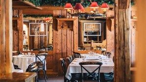 A restaurant interior with wooden walls, tables set with white tablecloths, and red pendant lights.