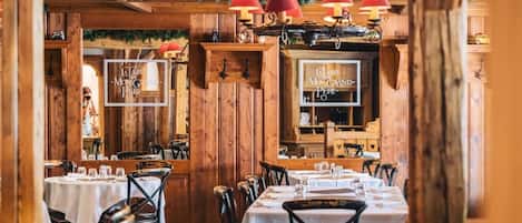 A restaurant interior with wooden walls, tables set with white tablecloths, and red pendant lights.