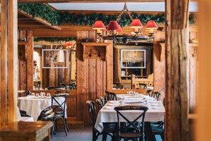 Een restaurant interieur met houten wanden, tafels gedekt met witte tafelkleden en rode hanglampen.