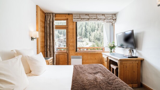 Une chambre  à coucher avec un lit, un bureau, une télévision et une fenêtre donnant sur une forêt.