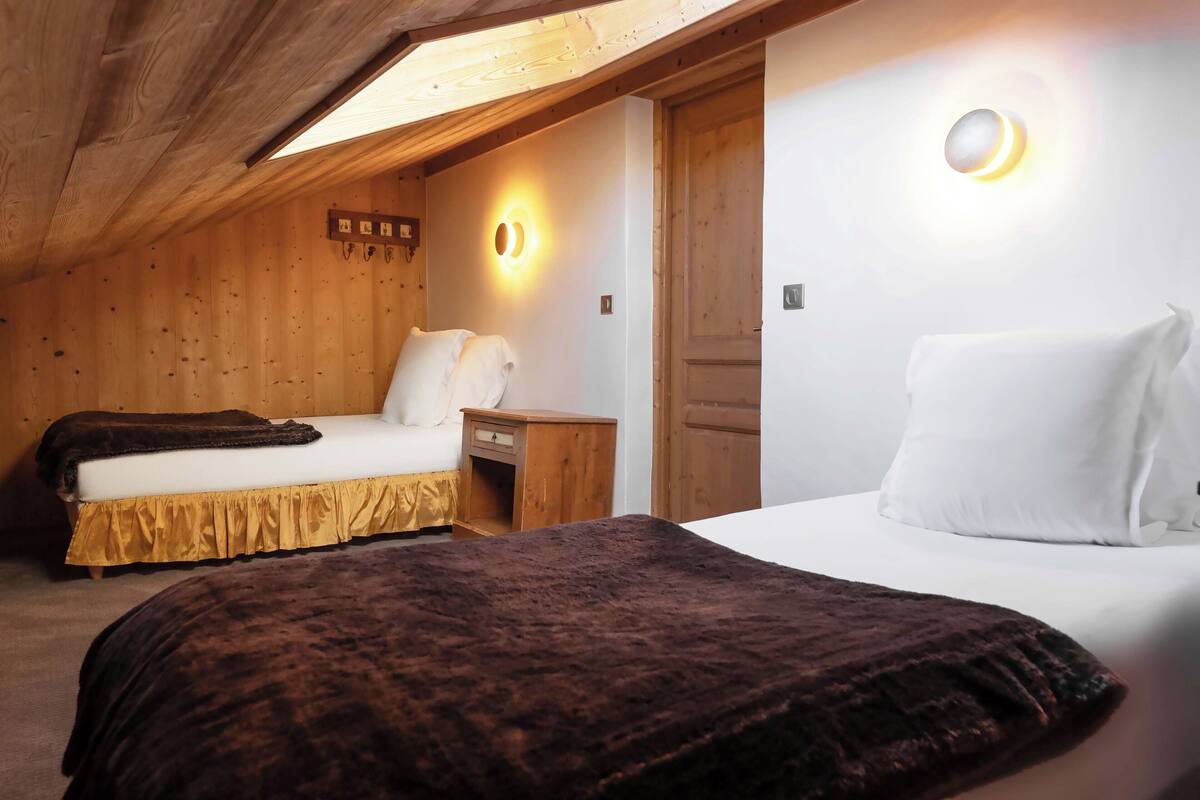 Een knus interieur met twee bedden, houten wanden, een klein houten nachtkastje en een wandlamp.
