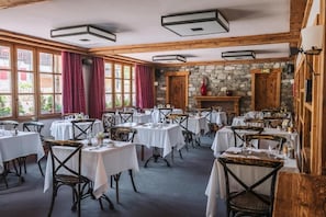 Um restaurante com várias mesas e cadeiras, uma parede de pedra e uma lareira.