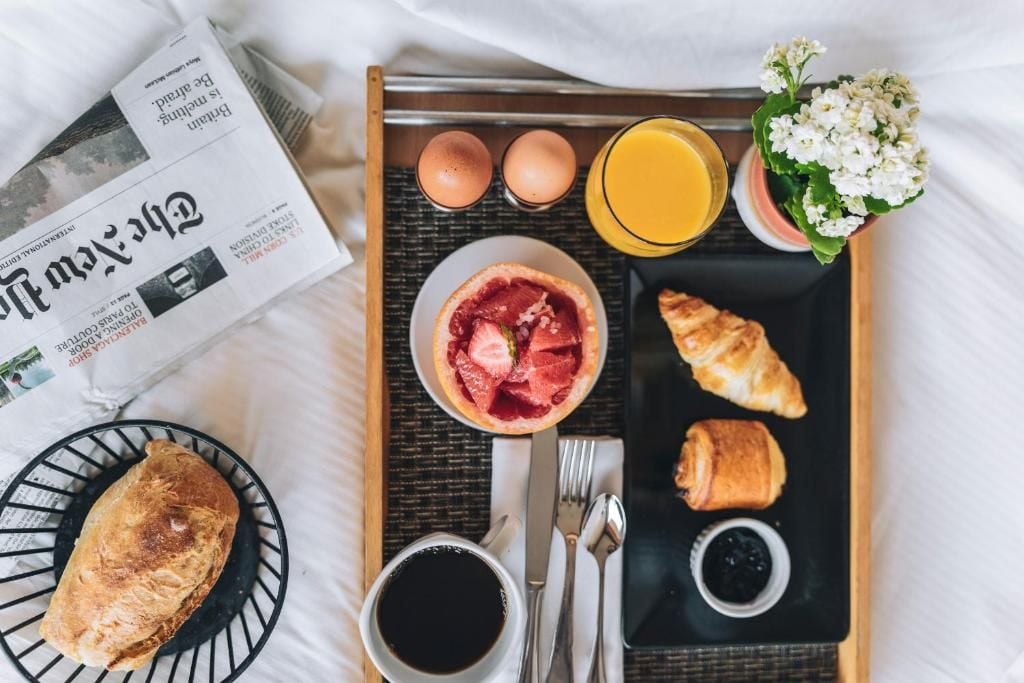A breakfast tray with croissants, a bowl of fruit, a glass of orange juice, and a newspaper.