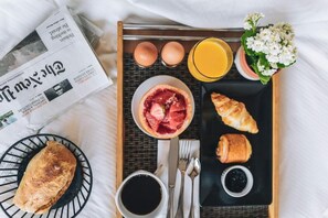 Un plateau de petit-déjeuner avec des croissants, un bol de fruits, un verre de jus d’orange et un journal.