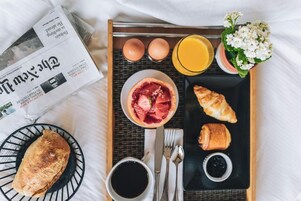 Un plateau de petit-déjeuner avec des croissants, un bol de fruits, un verre de jus d’orange et un journal.