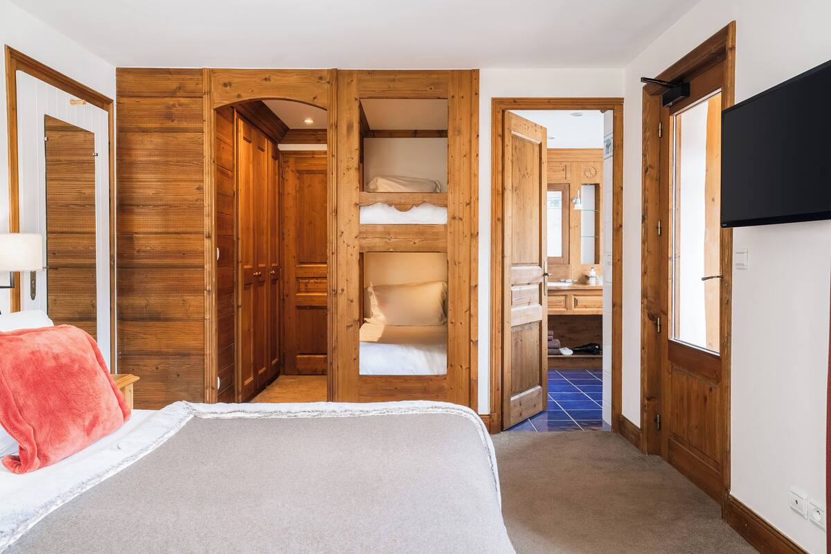 Een slaapkamer met een bed, een rode deken, houten kasten, een spiegel en een televisie.