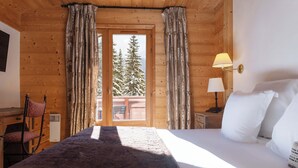 Une pièce de cabane en bois comprenant un lit, une chaise, une table et une fenêtre avec des rideaux.