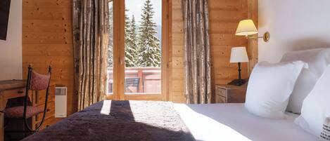 Une pièce de cabane en bois comprenant un lit, une chaise, une table et une fenêtre avec des rideaux.
