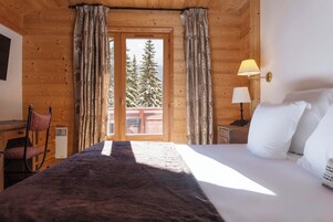 Une pièce de cabane en bois comprenant un lit, une chaise, une table et une fenêtre avec des rideaux.