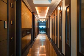 Un pasillo de hotel con piso reflectante, iluminación empotrada y puertas a ambos lados.