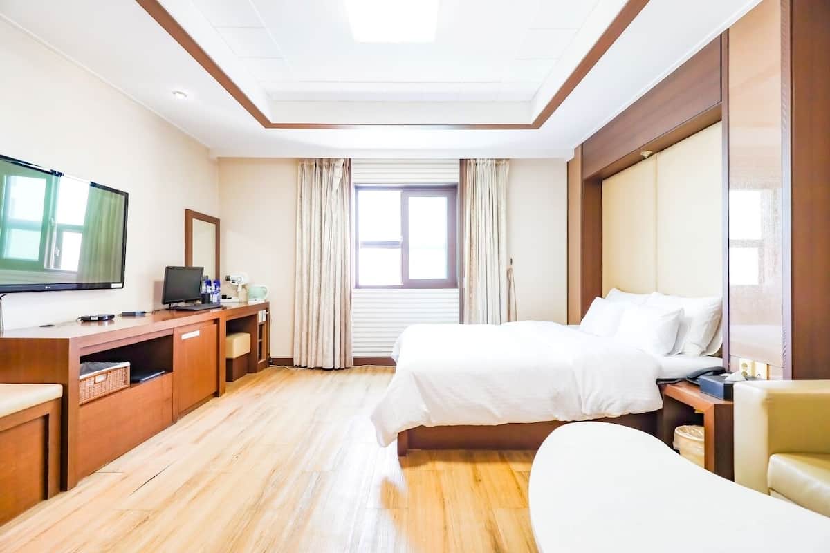 A hotel room with a bed, a desk with a computer, a television, and a window with curtains.