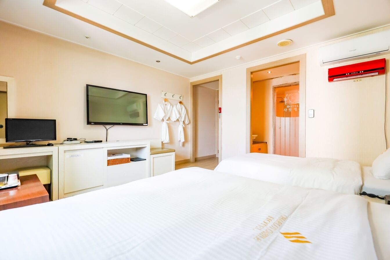 A hotel room with a bed, a desk with a television, a wardrobe, and a bathroom visible through an open door.