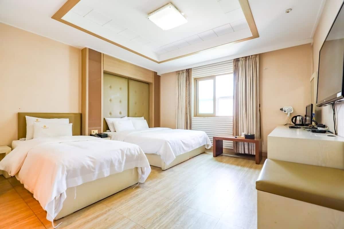 A hotel room with two beds, a desk, a TV, and a window with curtains.