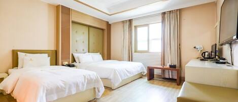 Een hotelkamer met twee bedden, een bureau, een televisie en een raam met gordijnen.
