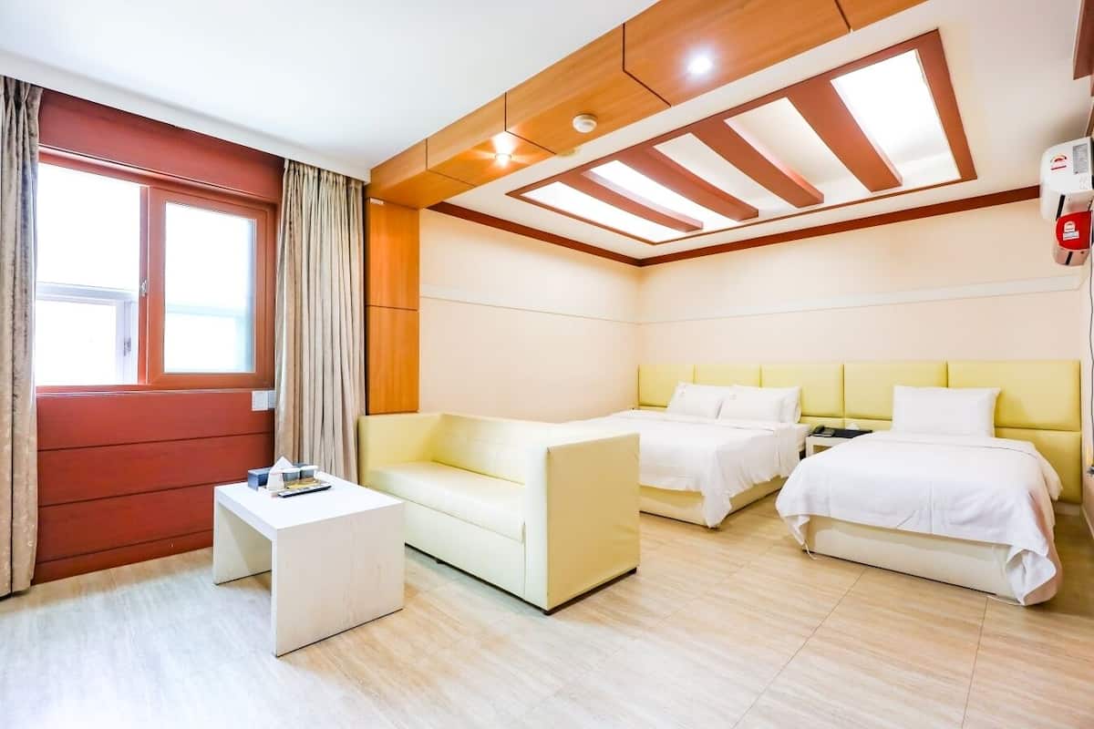 A hotel room with a bed, a sofa, a small table, and a window with curtains.