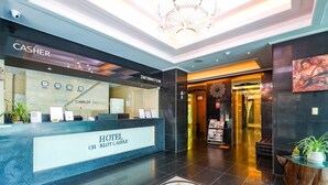 A hotel reception area with a modern design, including a reception desk labeled "HOTEL CHARLOT CASTLE," a cash register, and a chandelier. - Charlot Castle Hotel (Pyeongtaek)