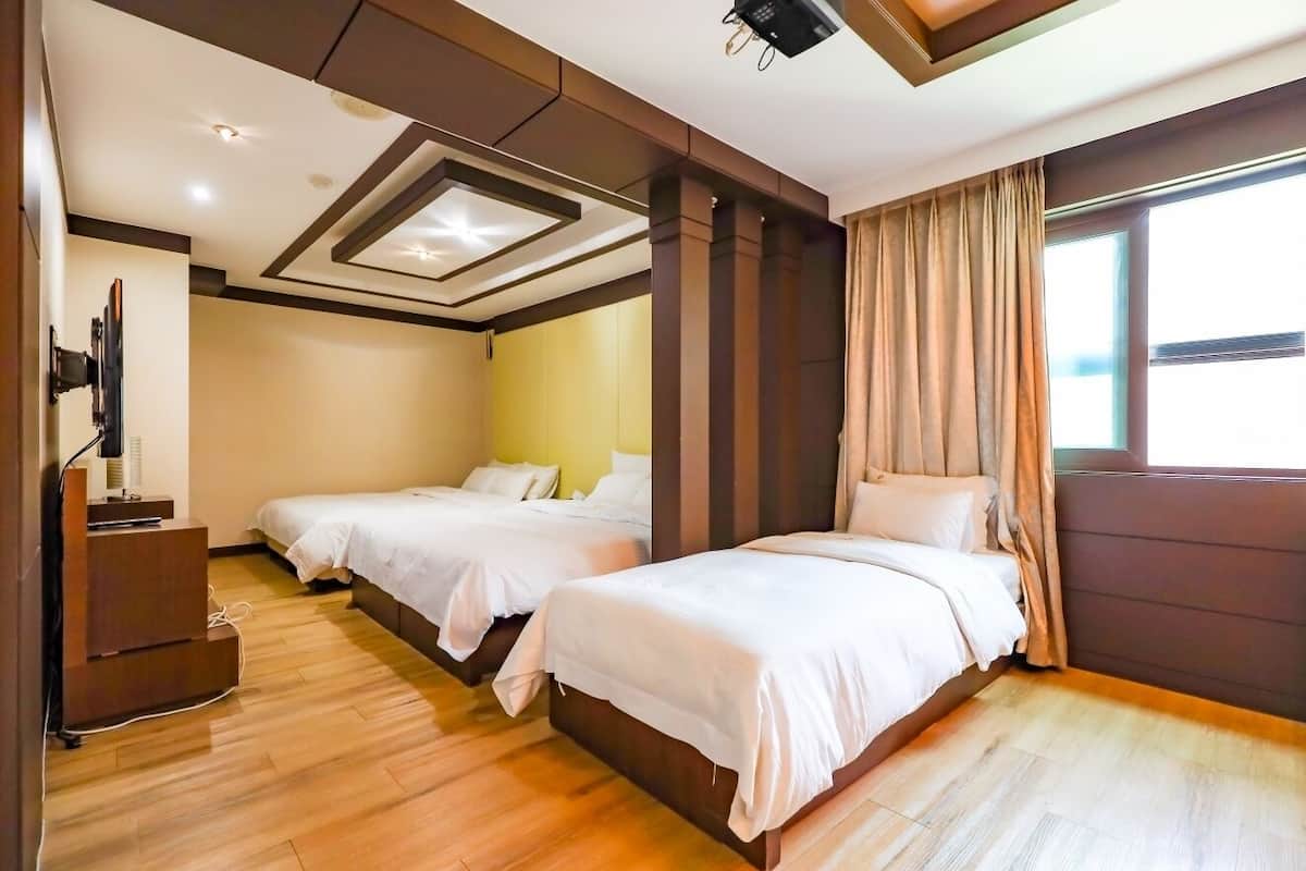 A hotel room with two beds, a TV, and a wooden floor.