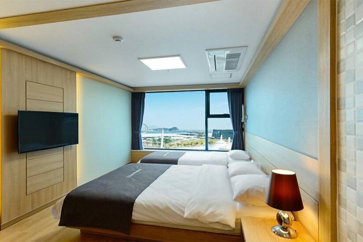 Ein Hotelzimmer mit einem großen Bett, einem an der Wand montierten Fernseher und einem Fenster mit Blick auf die Stadt.