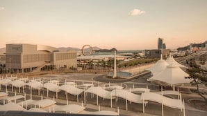 A modern urban area with a large building, a circular monument, and a unique white structure with a curved roof. - Paulownia Hostel & Guest House (Yeosu)