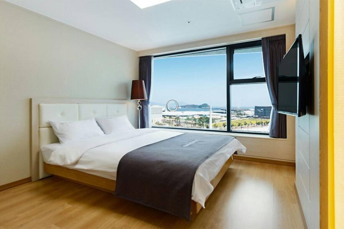 Ein modernes Hotelzimmer mit einem großen Bett, einem an der Wand montierten Fernseher und einem Fenster mit Blick auf die Stadt.