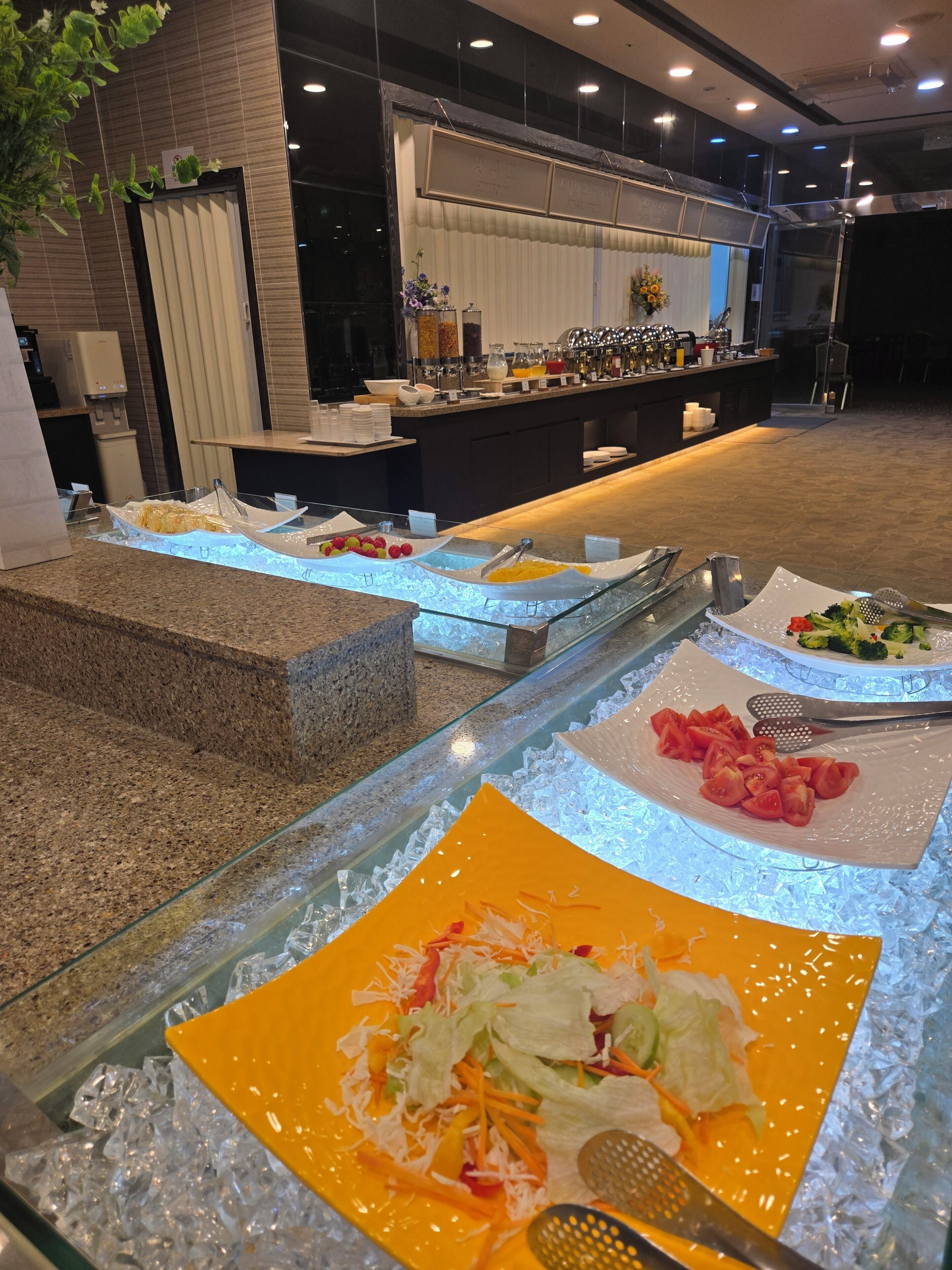Un buffet disposé avec différents plats présentés sur des plateaux réfrigérés, un distributeur d’eau et un espace détente offrant une vue sur le buffet.