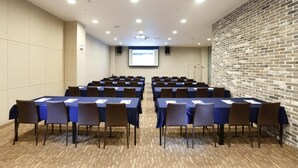 A conference room with rows of tables and chairs, a projector screen, and a brick wall. - Geosung Hotel (Eumseong)