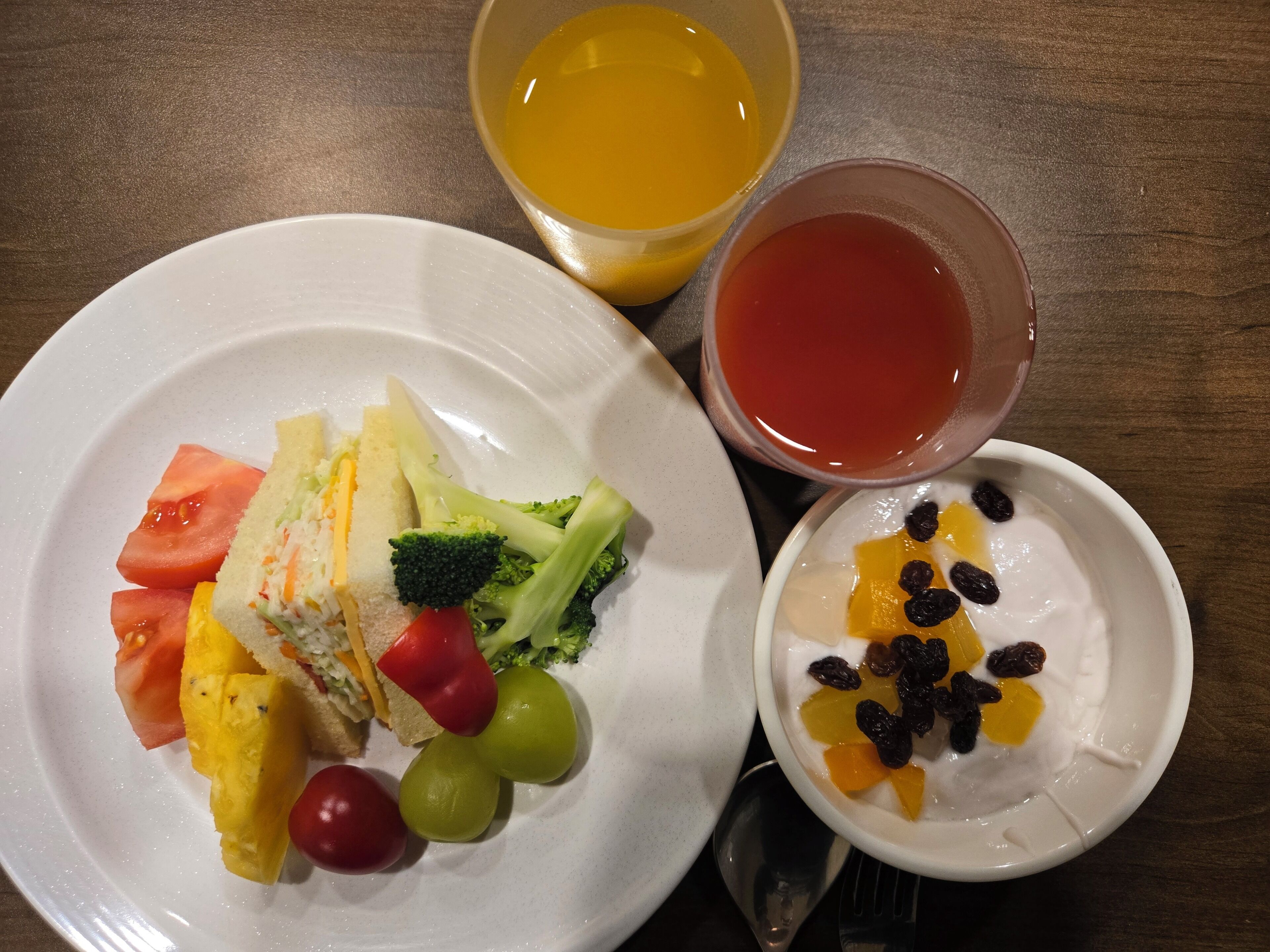 A plate with a sandwich, vegetables, and a bowl of fruit salad.