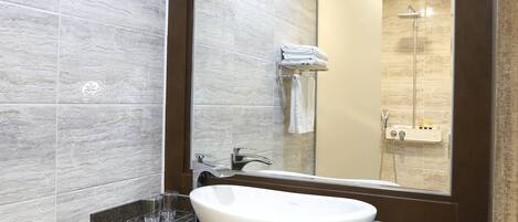 A modern bathroom with a large mirror, a white sink, and a shower area.
