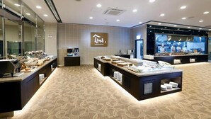 A modern hotel lobby with a buffet area, a reception desk, and a visible kitchen in the background. - Geosung Hotel (Eumseong)