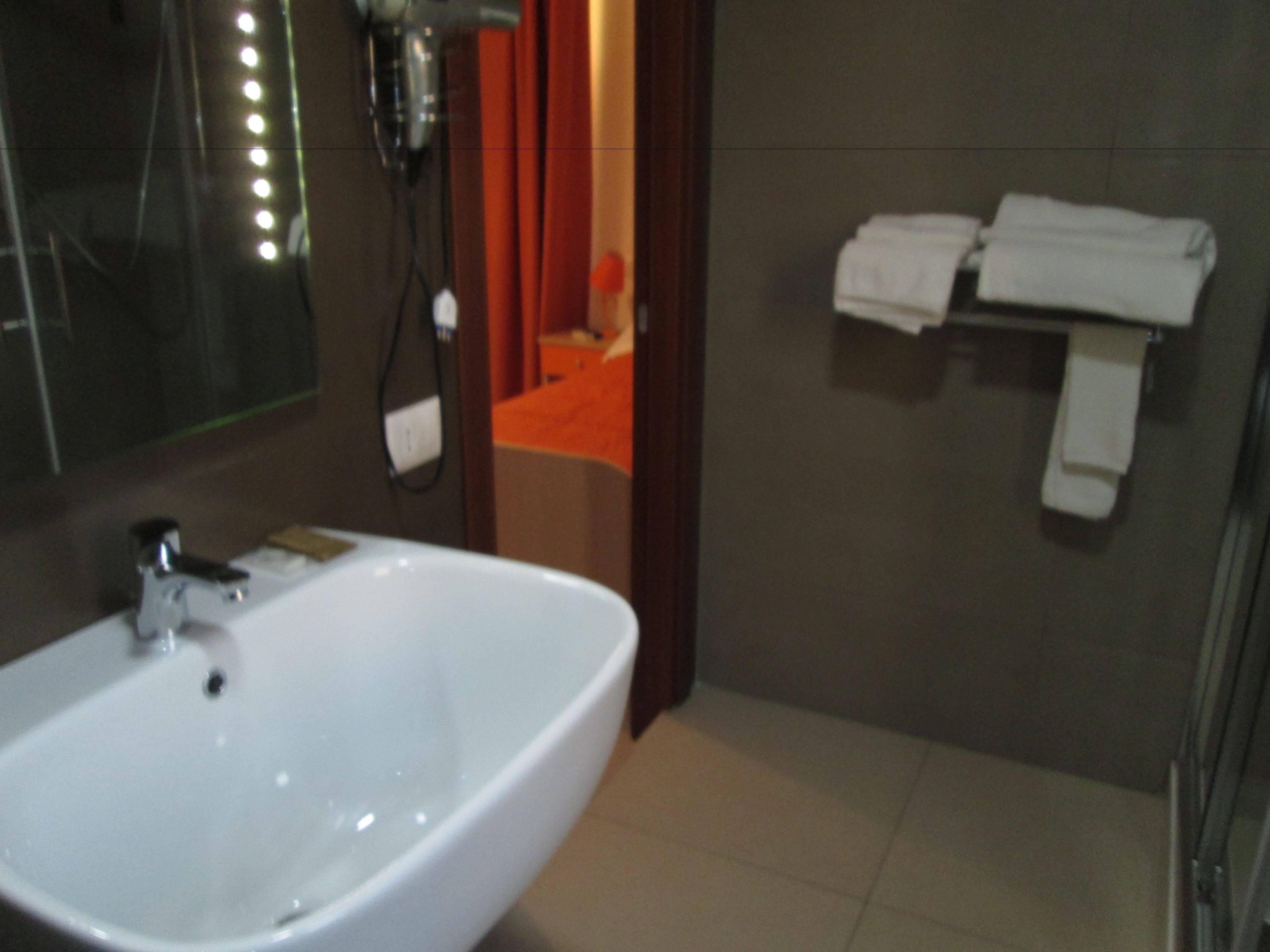 Un baño con lavamanos blanco, un espejo y un perchero con toallas.