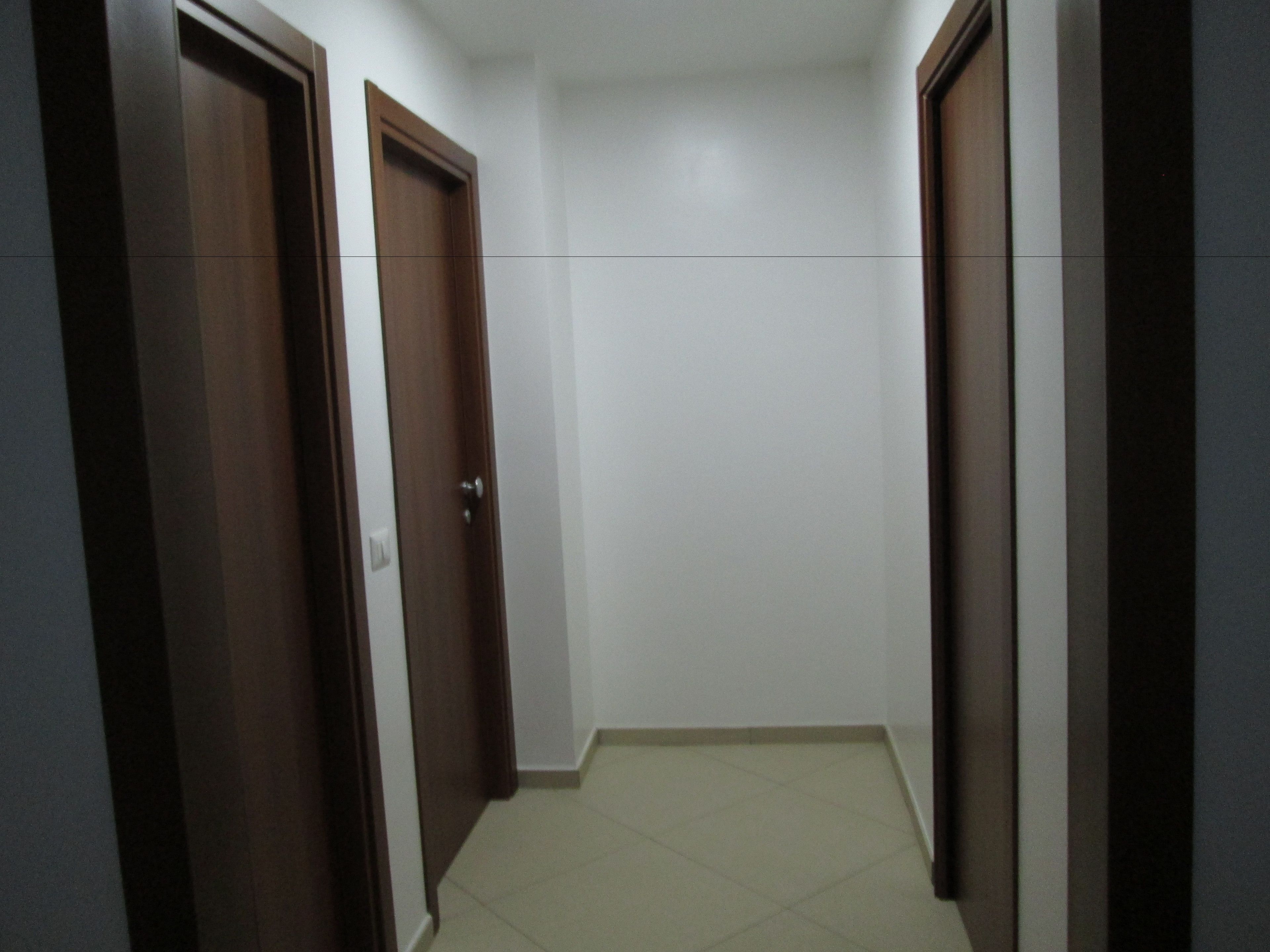 A narrow hallway with two wooden doors on either side and a tiled floor.