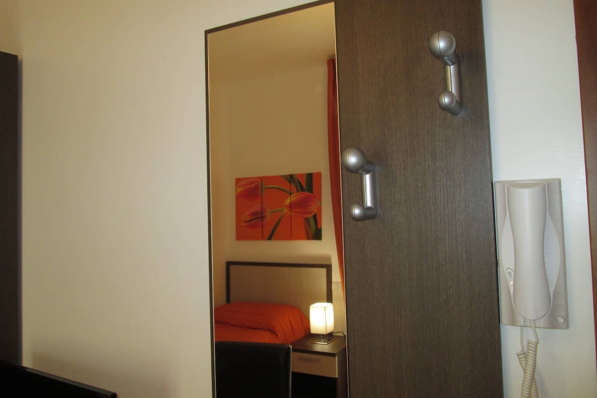A hotel room with a wooden door, a bedside lamp, a telephone, and a painting on the wall.