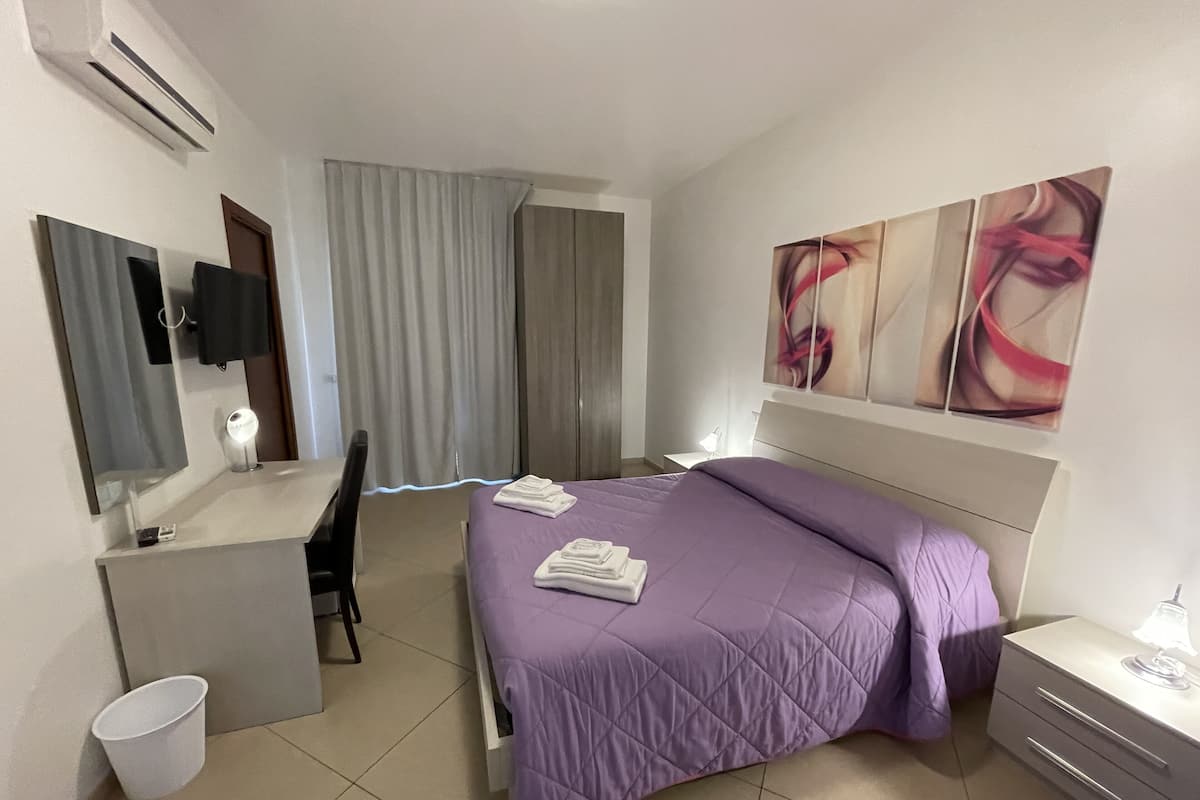 A hotel room with a bed, a desk, a chair, a mirror, and artwork on the wall.