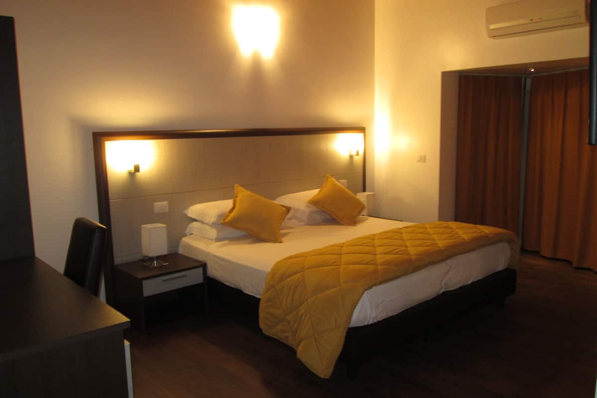 A hotel room with a bed, bedside tables, and an air conditioning unit.
