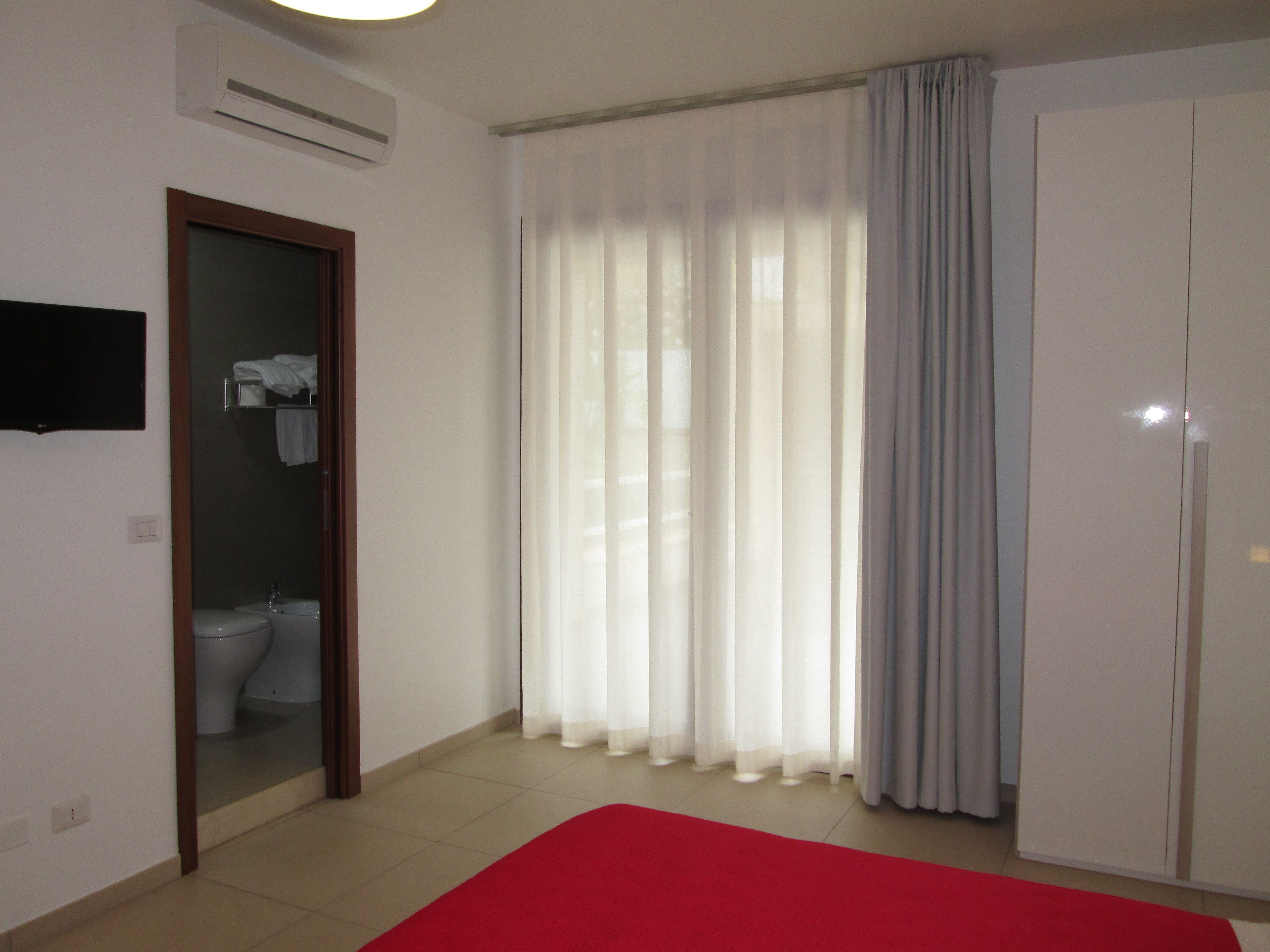 A room with a toilet, a sink, a red carpet, a wardrobe, and a TV mounted on the wall.