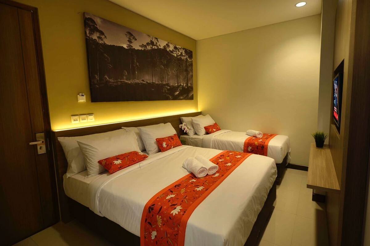 Ein Hotelzimmer mit zwei Betten, einem großen Gemälde an der Wand und einem kleinen Fernseher auf der rechten Seite.